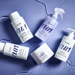 Color Wow Curl Produkte auf einer blauen, wasserähnlichen Oberfläche.