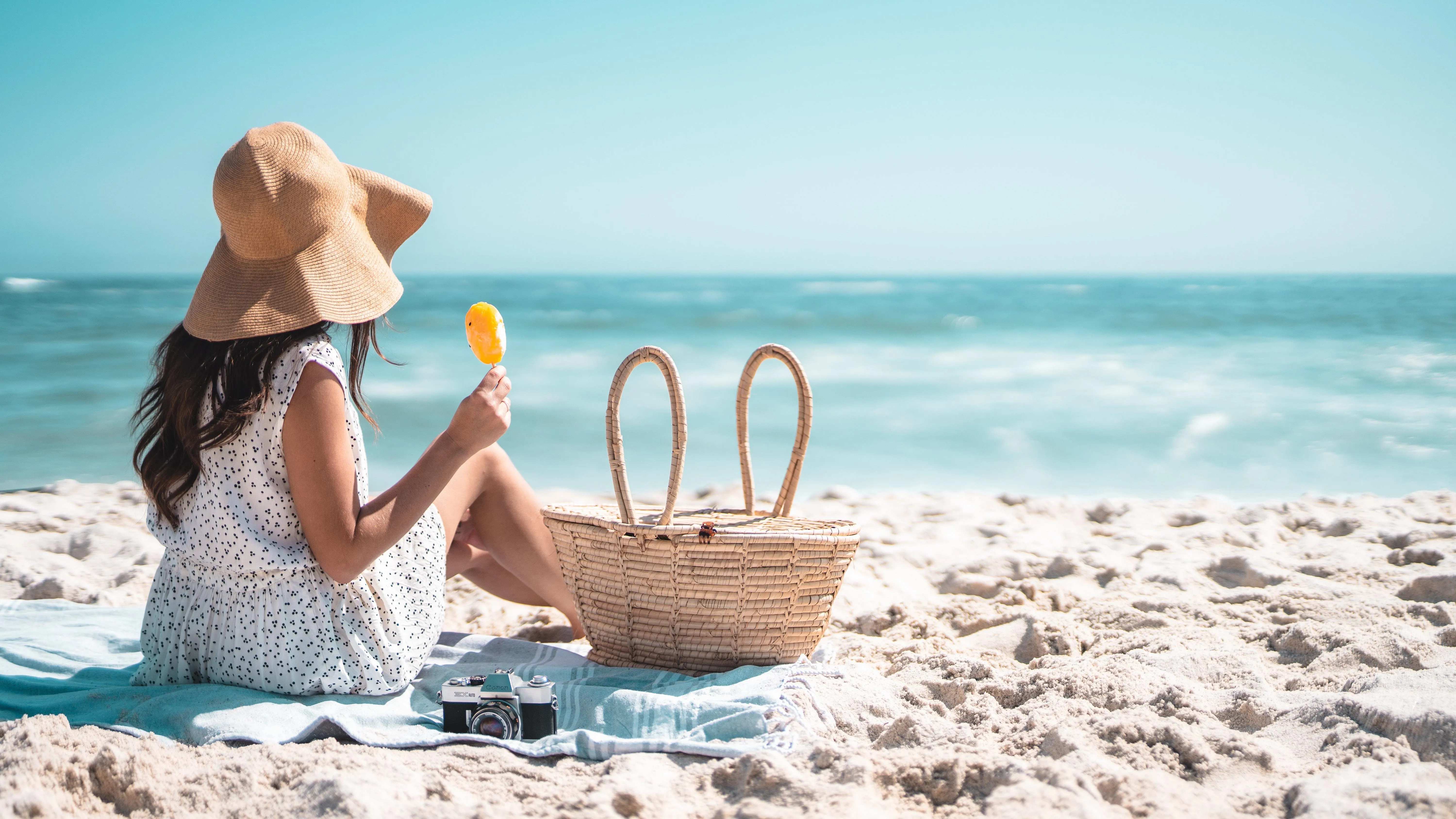 Kind mit Hut sitzt am Strand und isst ein Eis