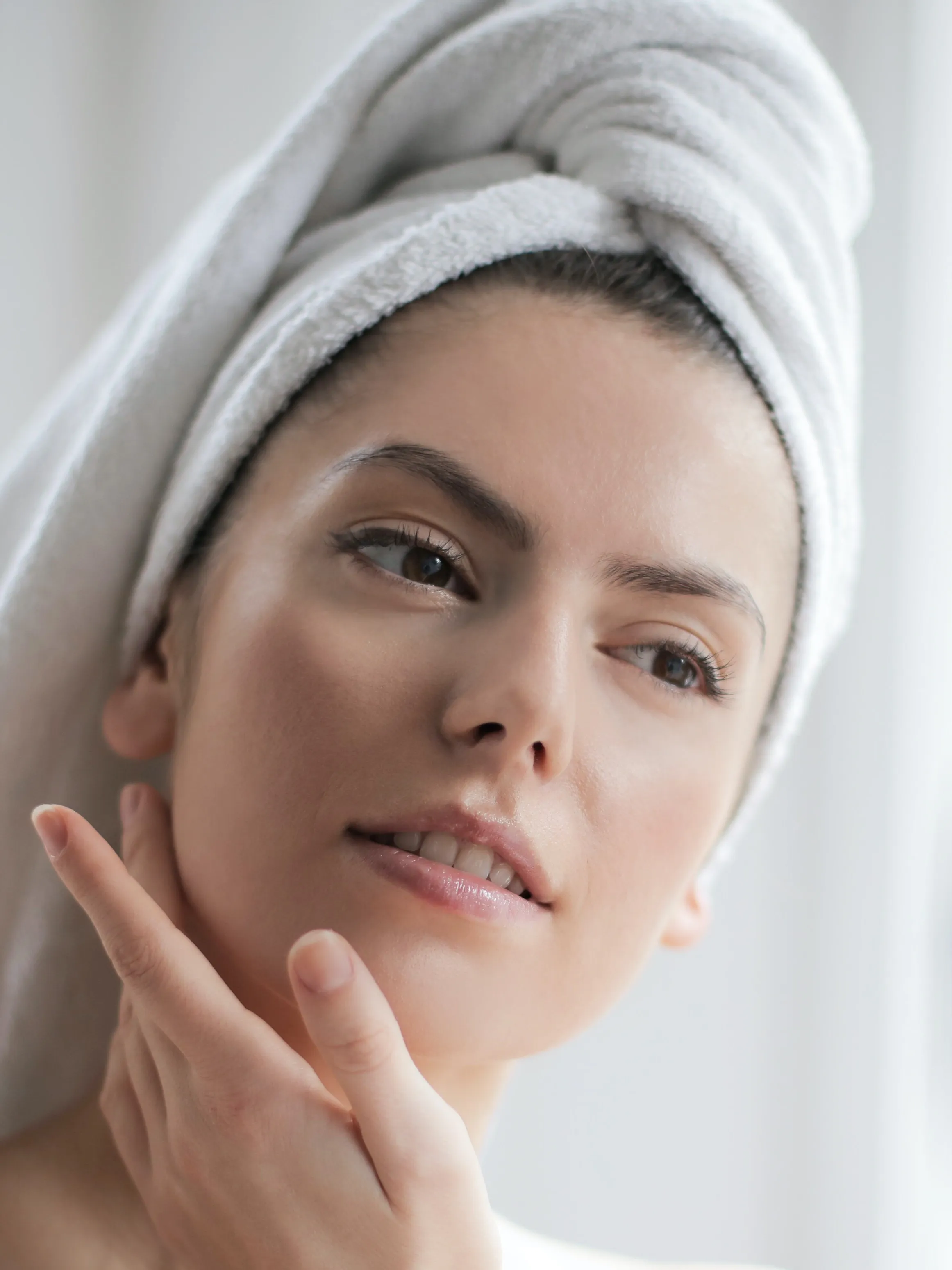 Frau mit Handtuch am Kopf betrachtet ihr Gesicht im Spiegel